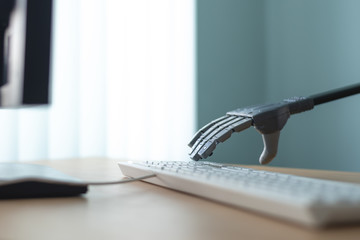 Robot with artificial intelligence is working on a computer. Robotic arm is pushing a keys on a computer keyboard.