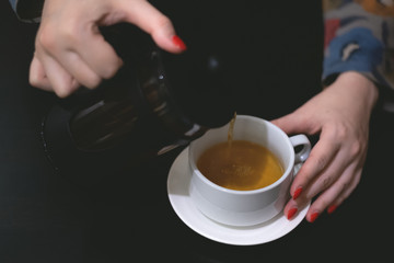 Woman is pouring a hot tea from teapot to a cup.
