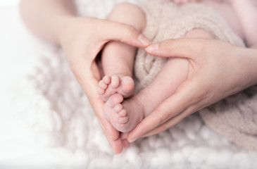 Winzige Babyfüße in den herzförmigen Händen der Mutter - obrazy, fototapety, plakaty