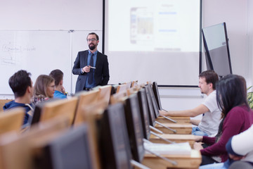 Group of students study with professor in modern school classroom. Male professor explain to...