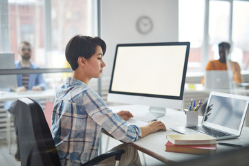 Obraz premium Young broker in casualwear looking at laptop display while sitting by desk and working by computer in office