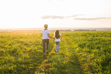 Rear view of mother and daughter running in green field with sunset on background