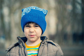 a boy in a winter hat grimaces and smiles in the Park . Face close-up