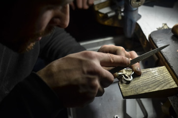 The master jeweler holds the working tool in his hands and makes jewelery at his workplace in the jewelry workshop.