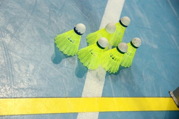 six bright yellow flounces on the floor of the playing field, blue background white and yellow line markings, badminton close-up