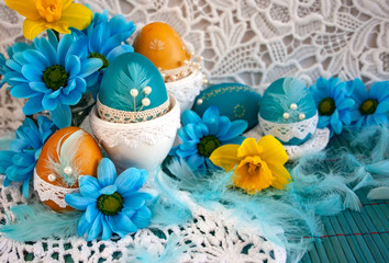 Wielkanocna kompozycja z niebieskiemi pisankami ozdobionymi koronką, żółtymi kwiatami, błękitnymi piórami © Monika