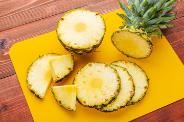 fresh ripe tropical pineapple cut into slices on a yellow rackside lying on a wooden table