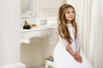 Portrait of cute little girl on white dress and wreath on first holy communion background church...