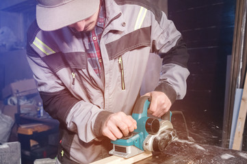 A young carpenter with a beard works with an electric plane without suctioning sawdust. Leveling and sanding wooden beams