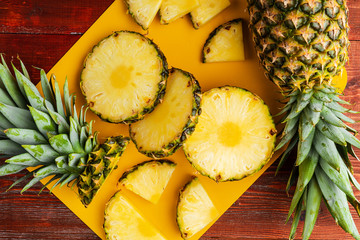 fresh ripe tropical pineapple cut into slices on a yellow rackside lying on a wooden table