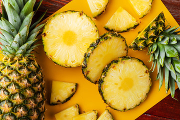 fresh ripe tropical pineapple cut into slices on a yellow rackside lying on a wooden table