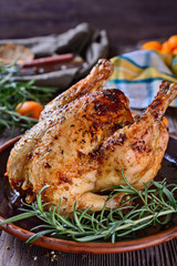 Delicious, freshly baked, crispy, baked chicken is appetizing served on a ceramic dish next to a sprig of fragrant rosemary