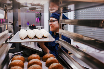 close up view of woman holding holding rack of rolls in a bakery.