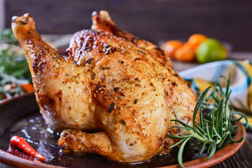 Delicious, freshly baked, crispy, baked chicken is appetizing served on a ceramic dish next to a sprig of fragrant rosemary