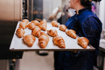 close up view of woman holding holding rack of croissants in a bakery.