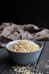 Rolled oats in ceramic bowl on dark wooden table with texture