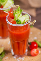 Two glasses of tomato juice decorated with fresh tomatoes, cucumber and leaves on a wooden background