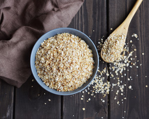 Rolled oats in bowl and spoon on dark wooden table, top view