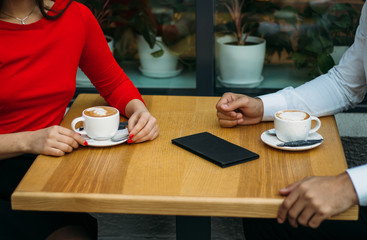 a couple, two, a guy and a girl are sitting in a cafe, drinking coffee, two cups of cappuccino on the table, bill for a drink. discussion
