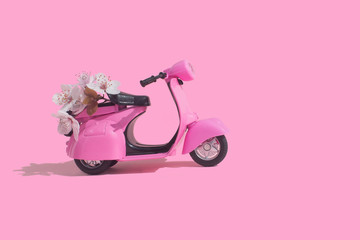 Pink retro toy bike delivering bouquet of flowers box on pink background. February 14 card, Valentine's day. Flower delivery. 8 March, International Happy Women's Day. Mother's day