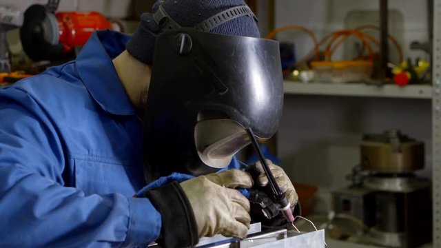 A man puts on a welder mask and starts welding in a workshop, professional welder.