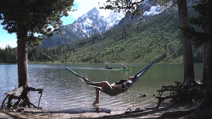 Man napping in a hammock next to a lake with mountains in the distance at Grand Teton National Park, Wyoming