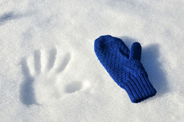 Wool knitted downy soft warm white patterned mitten lies on white snow in sunny weather. Handprint with fingers in the snow. The concept of the completion of winter and the onset of spring.