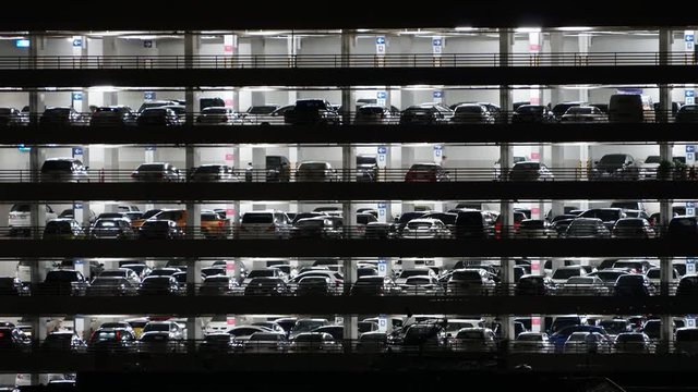 A night timelapse shot of a multilevel garage with lots of cars parking and leaving the place.