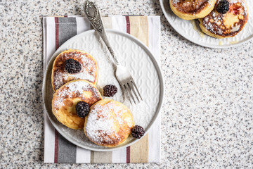 Homemade curd fritters with berries and a cup of milk on a gray background. Healthy and diet breakfast