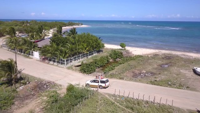 Car drives along rough road next to beach in Dominican Republic, viewed by drone, with sea in the background