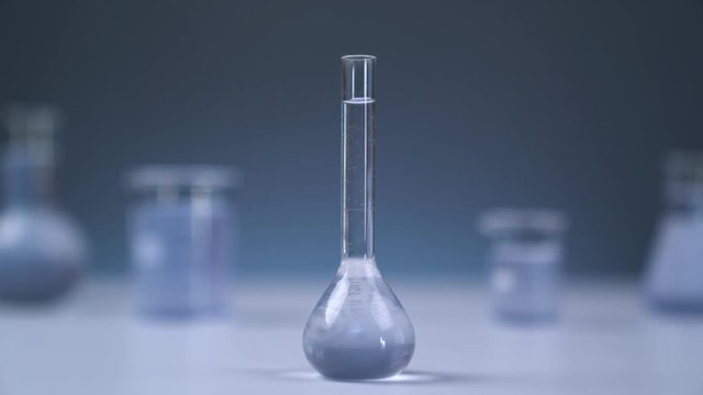 On the table is a medical flask with liquid. The camera smoothly leaves the flask. Gray wall on background. Flasks in defocus on the gray background.