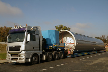 A view of a truck, a low-loader semi-trailer and an oversized cargo in the parking lot.