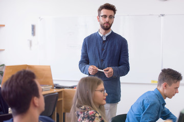 Group of students study with professor in modern school classroom. Male professor explain to...