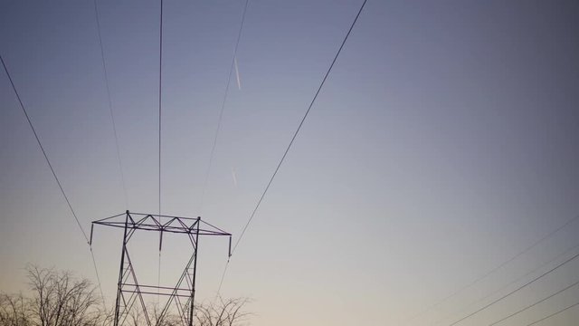 Shot below hydro lines looking up at the winter sky of two airplanes high in the sky with jet trails.