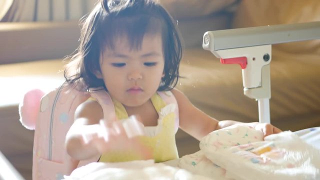 Little Asian baby girl, 22 months old, playing / learning to arrange / stack up her diapers in pile