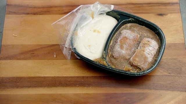 Icy frozen meal food in a black container being dropped sideways on the dining table 
(medium shot)
