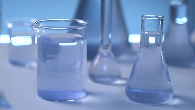 On the table is a medical flask with liquid. The camera smoothly leaves the flask. Gray wall on background. Flasks in defocus on the gray background.