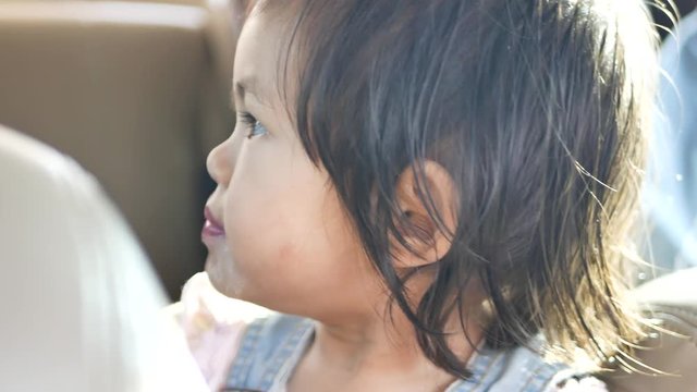 Little Asian baby girl, 22 months old, enjoys eating ice cream in a car