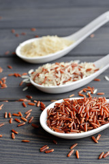 Mixed organic raw rice in ceramic spoons over dark desk background