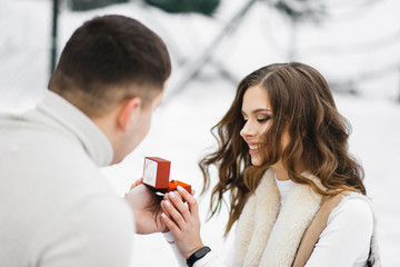 Winter love story on ice. The guy offers to marry a girl standing on his knee in the hands of a wedding ring on the ice on the skates