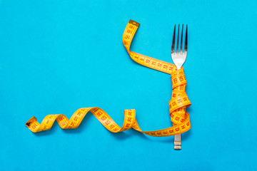 Tape measure around a fork as concept for diet. Fork are wrapped in yellow measuring tape on blue...