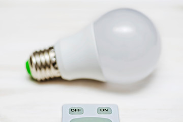LED light bulb and remote control with buttons on and off on a white wooden background