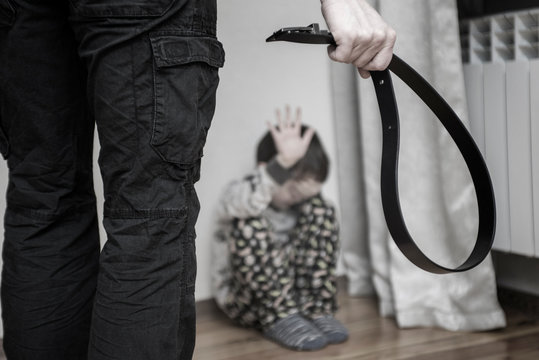 Aggressive parent with belt and frightened child in corner. Domestic violence. Abused child, aggression in the family