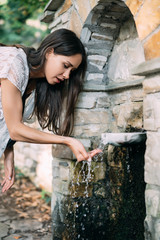 Beautiful, young girl drinks spring water outdoor