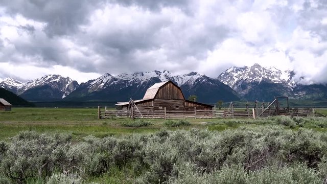 Slow pan of Moulton Barn on a stormy day with snowy mountains on Mormon Row in Grand Teton National Park, Wyoming