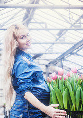 Pregnant beautiful woman works at greenhouse with flowers.