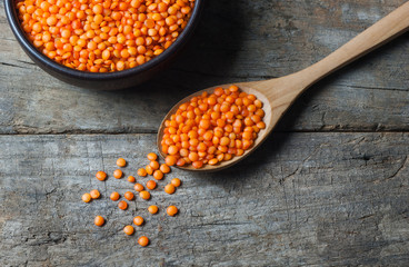 Red lentils in wooden spoon on wooden background. Uncooked red lentil legumes, herbaceous plant (Lens culinaris) in bowl