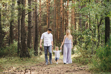 Naklejka na ściany i meble Happy young family spends time together in nature. Parents go and hold the child's hands