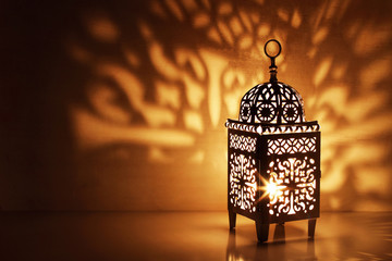 Silhouette of Moroccan ornamental lantern with burning glowing candle. Decorative shadows. Festive greeting card, invitation for Muslim holy month Ramadan Kareem. Festive night background.