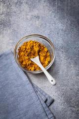 Turmeric powder in glass bowl with spoon on gray grunge background